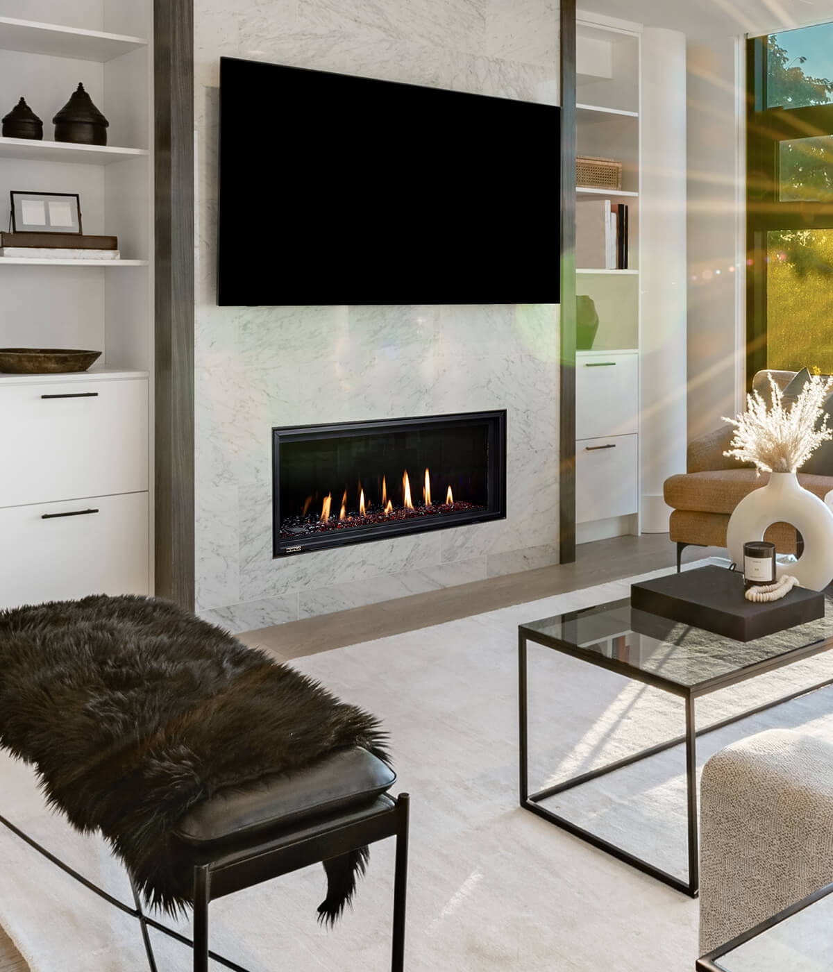 Montigo DelRay Linear gas fireplace set into a honed marble surround with a television mounted directly above, in a contemporary living room with built-in shelving