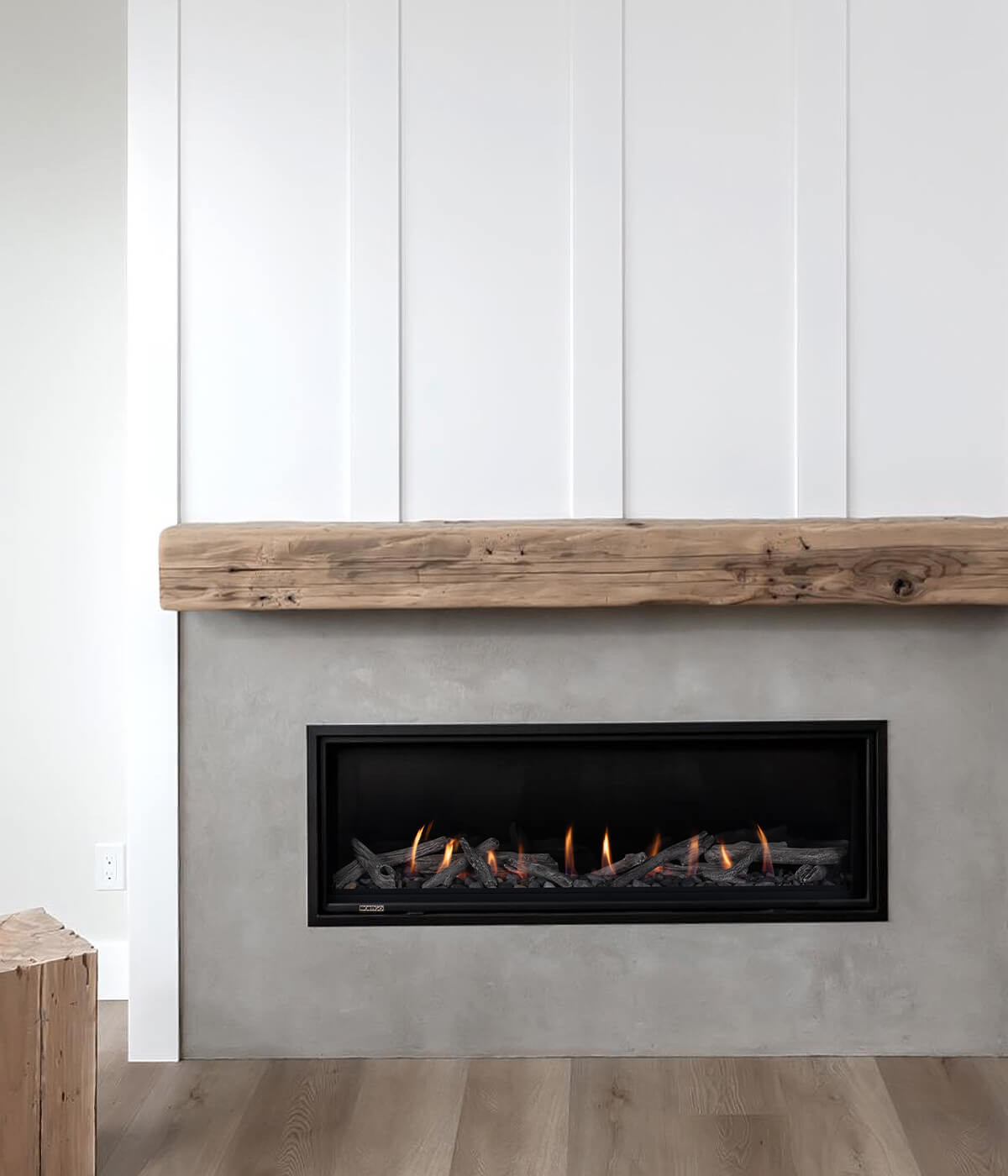 Montigo DelRay Linear gas fireplace with a realistic log set, set into a smooth concrete surround beneath a chunky reclaimed-wood mantel and white board-and-batten panelling