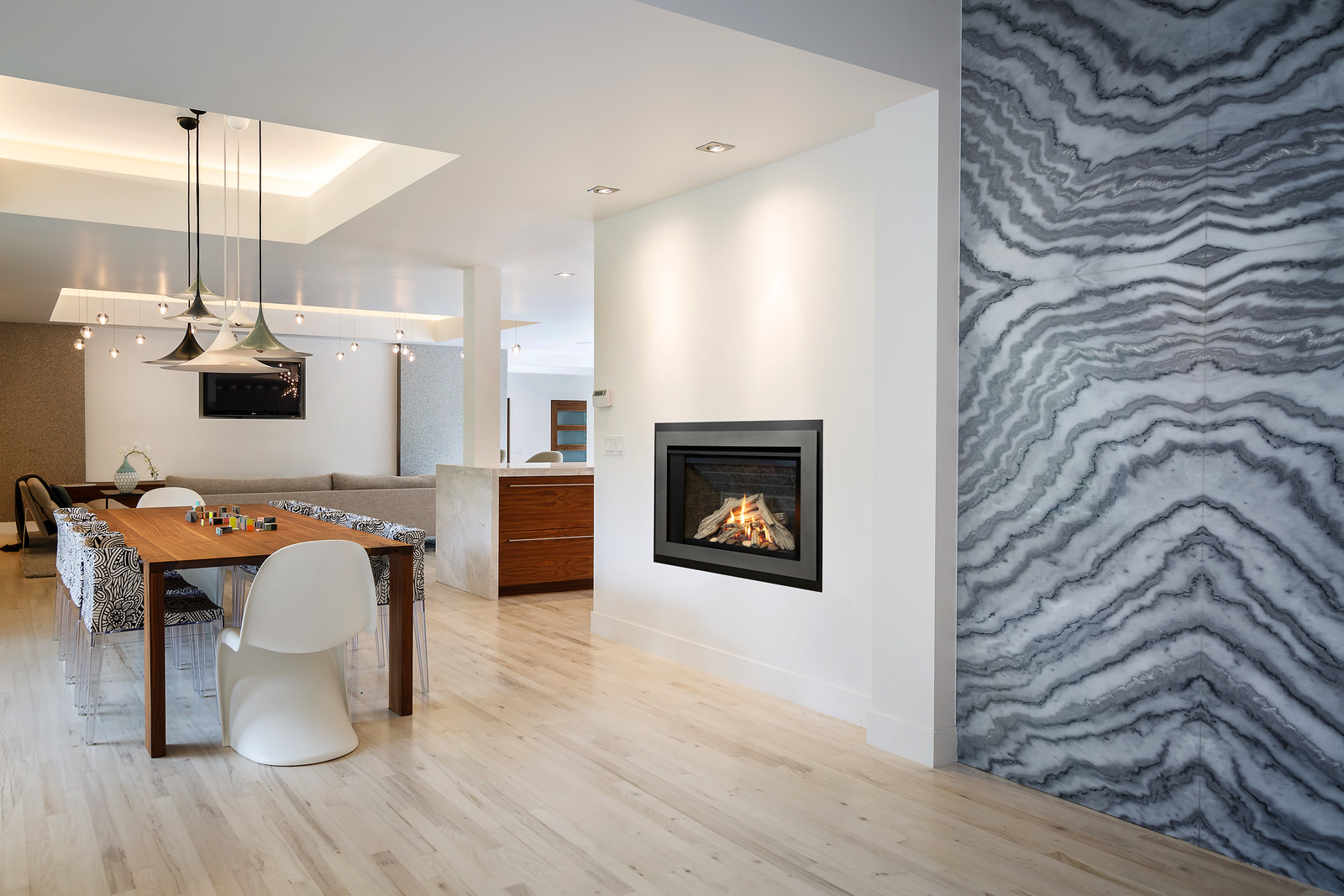 Valor H3 radiant gas fireplace set into a white wall beside a dramatic grey marble feature wall, in an open-plan dining and living room with pale wood floors