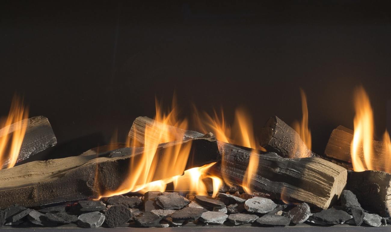 Close view inside an Element4 gas firebox — tall amber flames rising between and around true-to-nature cleaved wood logs set on a bed of dark lava stone, against the black rear panel of the fire