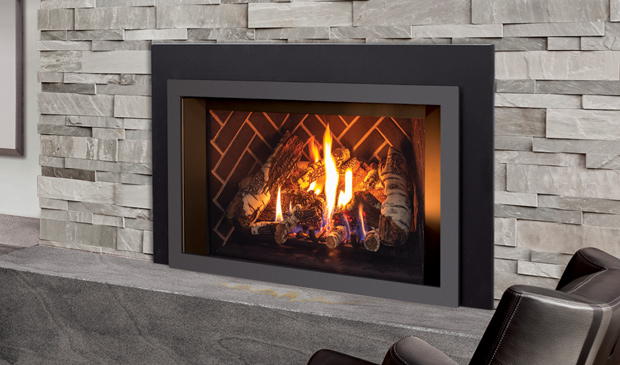 Enviro E33 gas insert with a black contemporary surround set into a grey stacked-stone fireplace above a slate hearth, a log fire on a herringbone liner, a leather armchair beside it