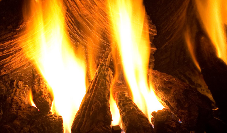 Close view of an Enviro gas insert’s flames rising between charred ceramic logs, orange and yellow fire filling the frame