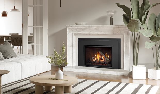 Enviro Ri30 gas insert with a black surround set into a white marble fireplace in a bright living room, a white sofa, a round oak coffee table and a tall bird-of-paradise plant beside it