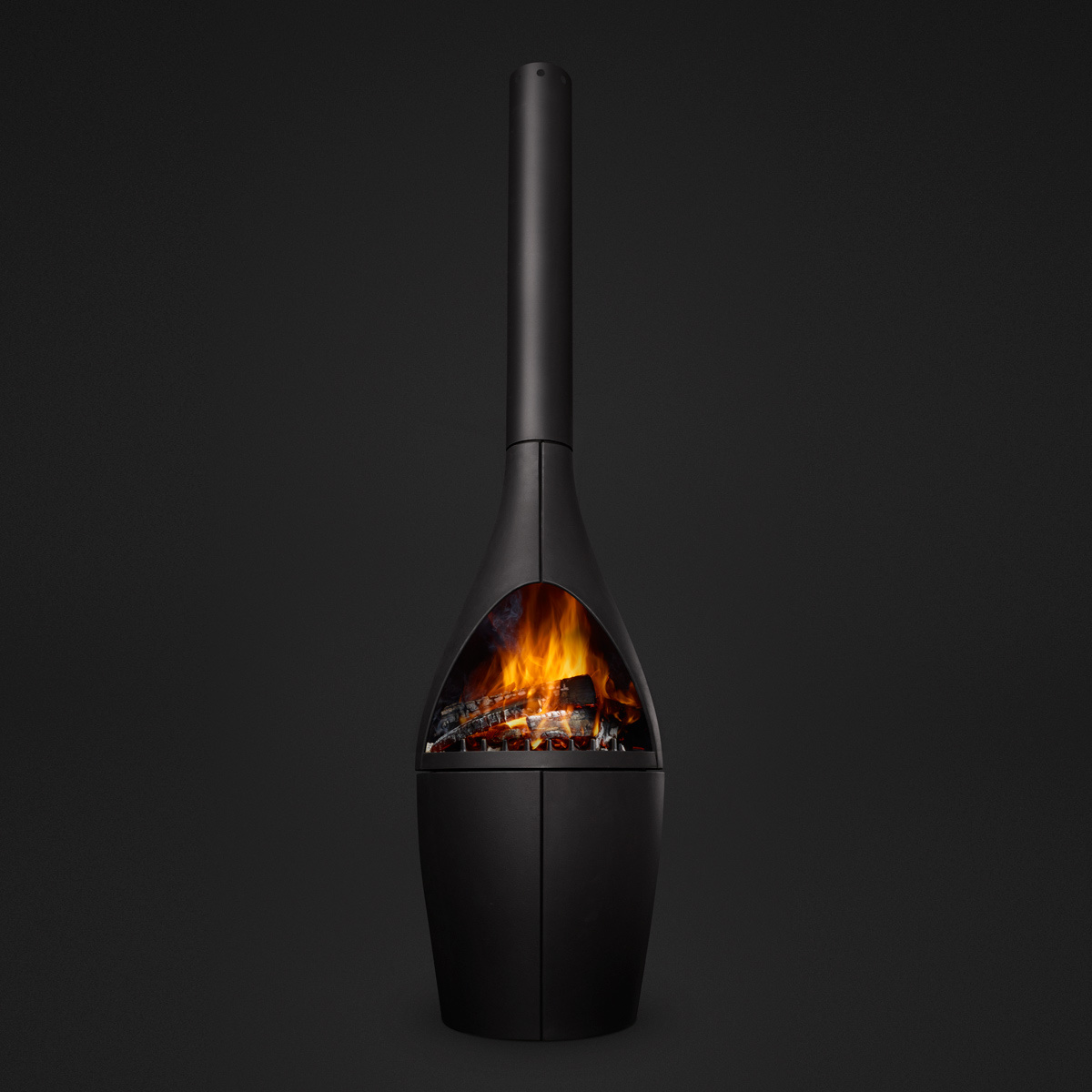 Morsø Kamino outdoor fireplace photographed on a dark background, full cast iron silhouette with a glowing fire inside