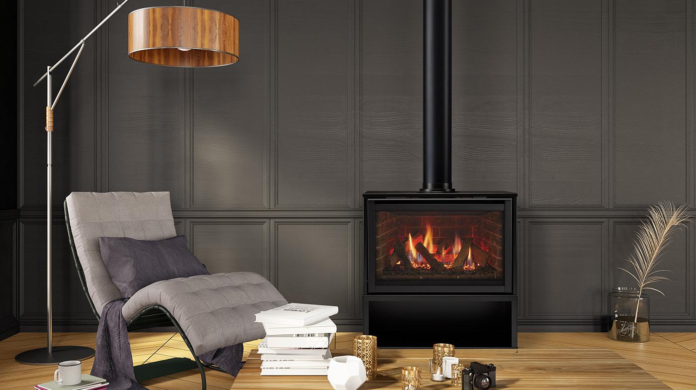Majestic Ruby freestanding gas fireplace against a dark panelled wall, a log fire in front of brick-pattern interior panels, with a lounge chair, a floor lamp and a stack of books beside it