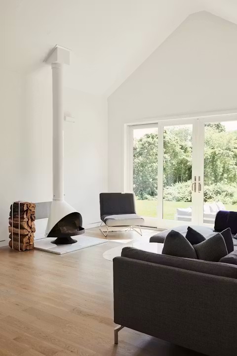 Malm 34 Zircon DV cone fireplace in a bright living room with a vaulted ceiling, white walls, a gray sofa and a stacked log holder beside the fireplace