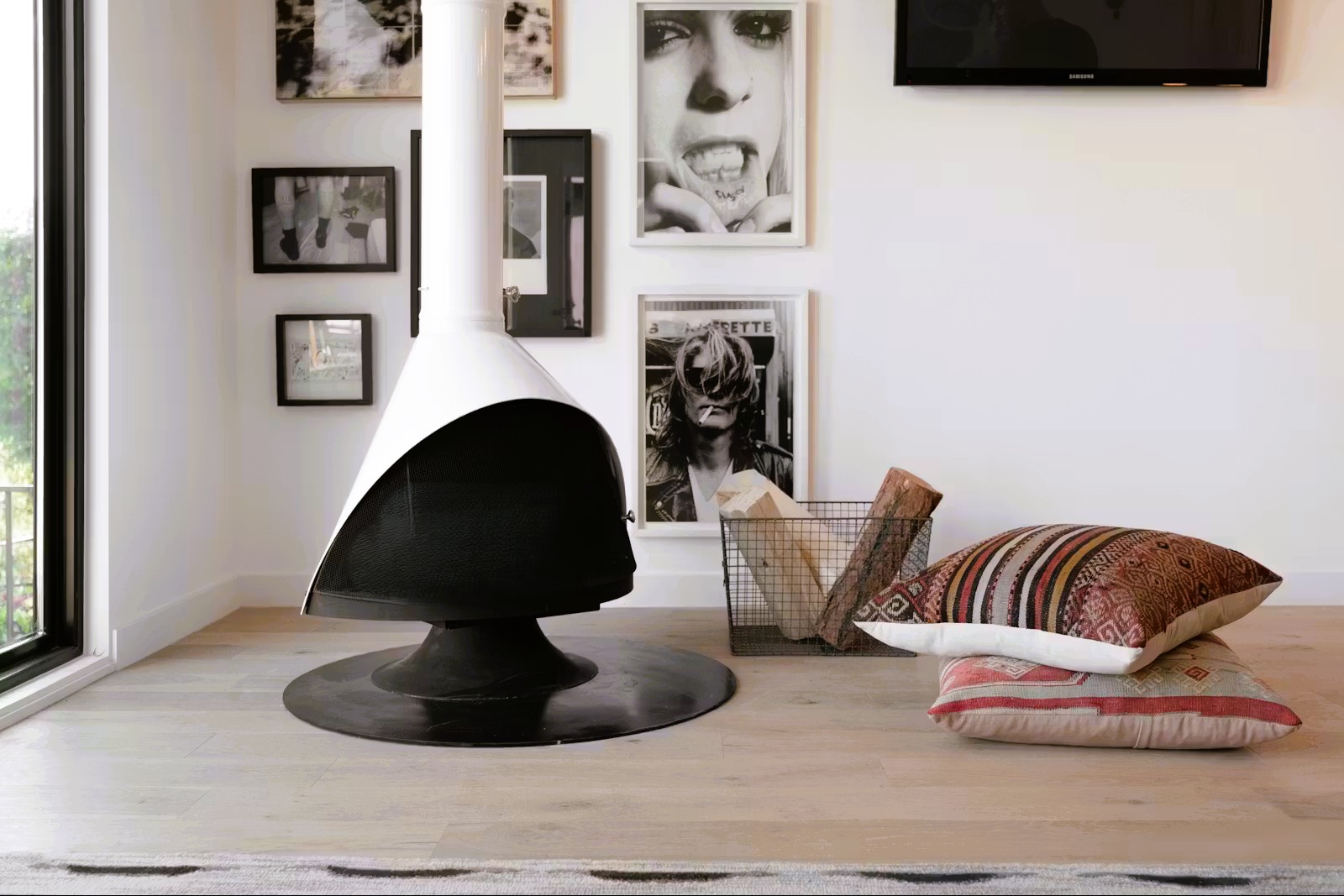 Malm 34 Zircon DV cone fireplace in a loft apartment surrounded by a wall of black-and-white framed portrait photographs, with kilim cushions on the floor
