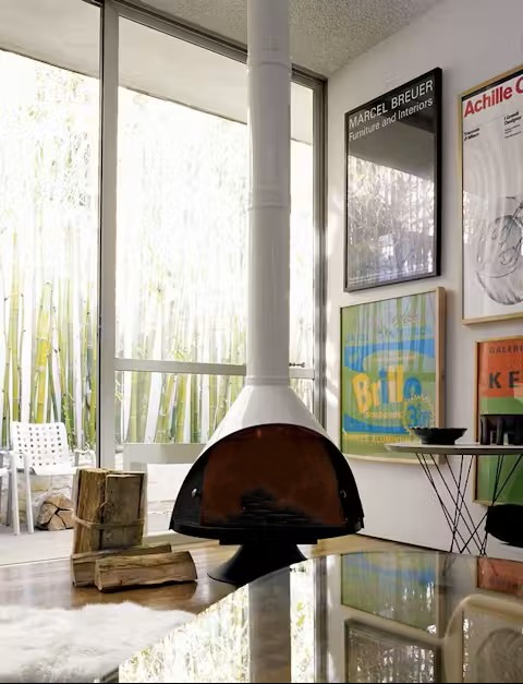 Malm 34 Zircon DV cone fireplace in a designer's studio with bamboo visible through floor-to-ceiling windows and framed Marcel Breuer and Castiglioni furniture posters on the wall