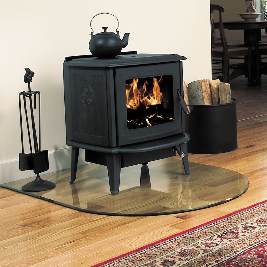 Morsø 7110 cast-iron wood stove with a wide bar-free glass door and a kettle on top, lit on a patterned rug in a panelled room