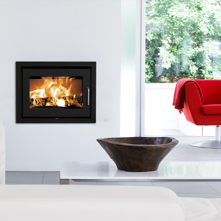 Morsø 5660 cast-iron wood-burning insert set flush into a white wall with a wide fire behind the glass, in a bright, minimalist modern room