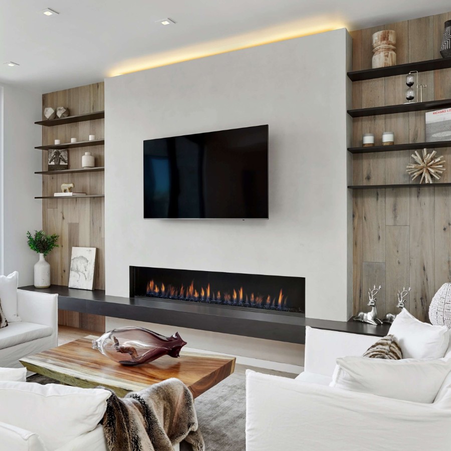 Ortal linear gas fireplace set in a pale plaster feature wall with a television mounted directly above the fire, flanked by wood shelving and styled with white sofas and a live-edge timber coffee table