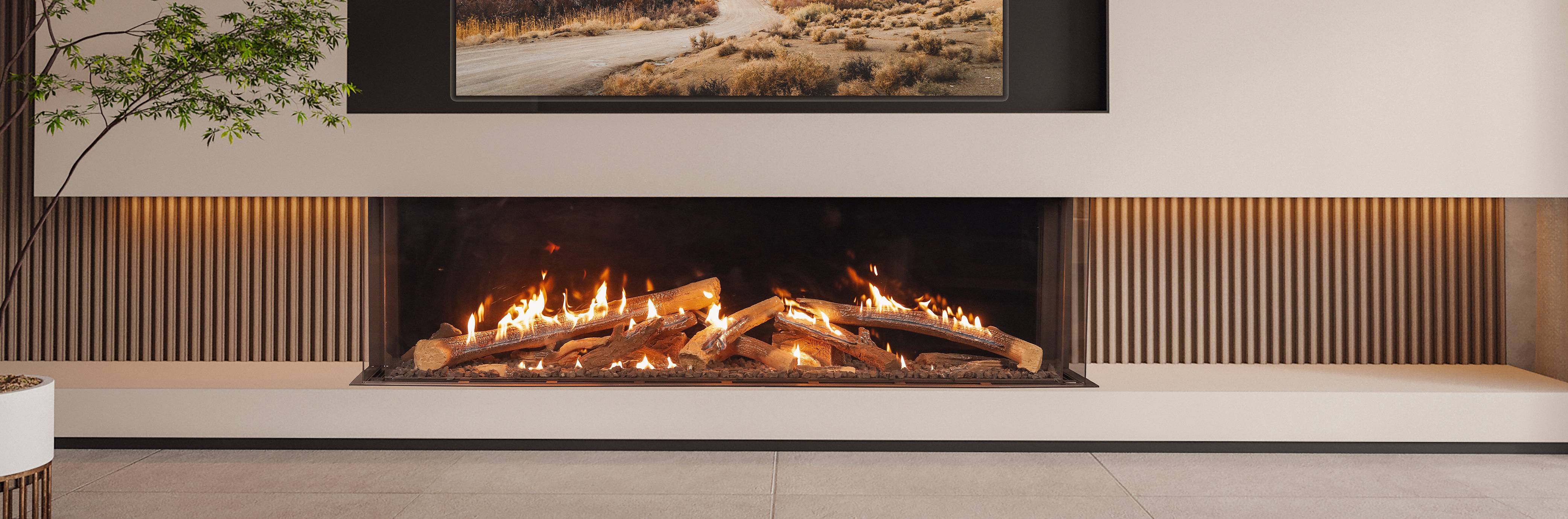 Wide Ortal three-sided gas fireplace running the full length of a wood-slat feature wall, a long panoramic plane of flame over a driftwood log bed with framed landscape art mounted directly above it