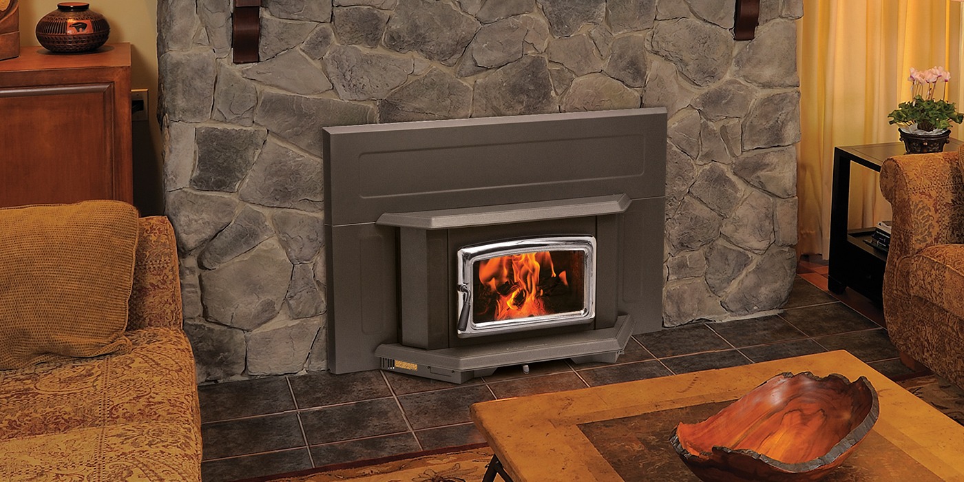 Pacific Energy Summit Insert LE in a bronze finish with a nickel door set into a grey fieldstone fireplace with a tiled hearth, armchairs on either side
