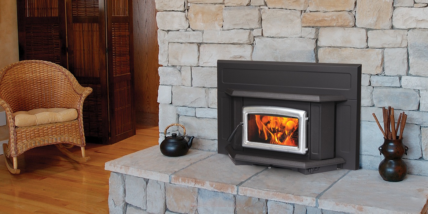 Pacific Energy Super Insert LE with a nickel arched door set into a pale limestone fireplace with a raised stone hearth, a wicker rocking chair beside it