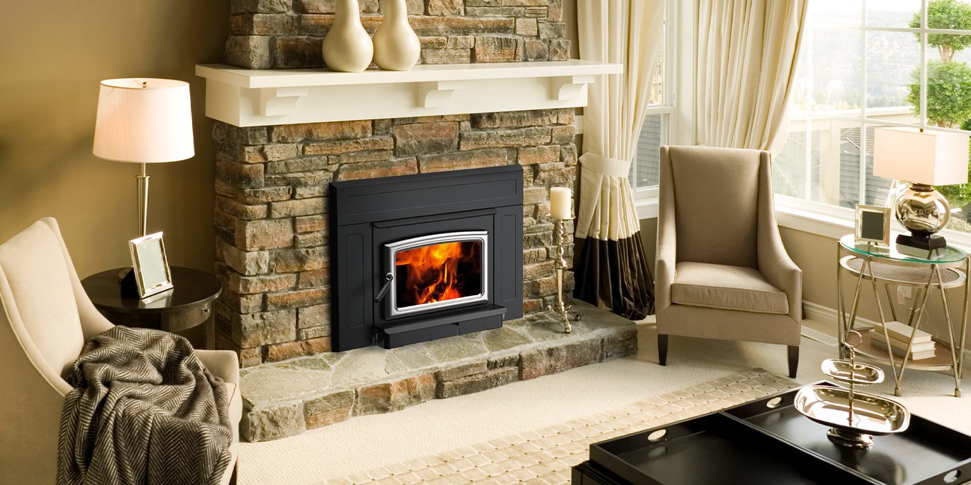 Pacific Energy Vista Insert LE2 with an arched nickel door set into a stacked-stone fireplace beneath a white mantel, in a pale living room with wing chairs, table lamps and tall curtained windows