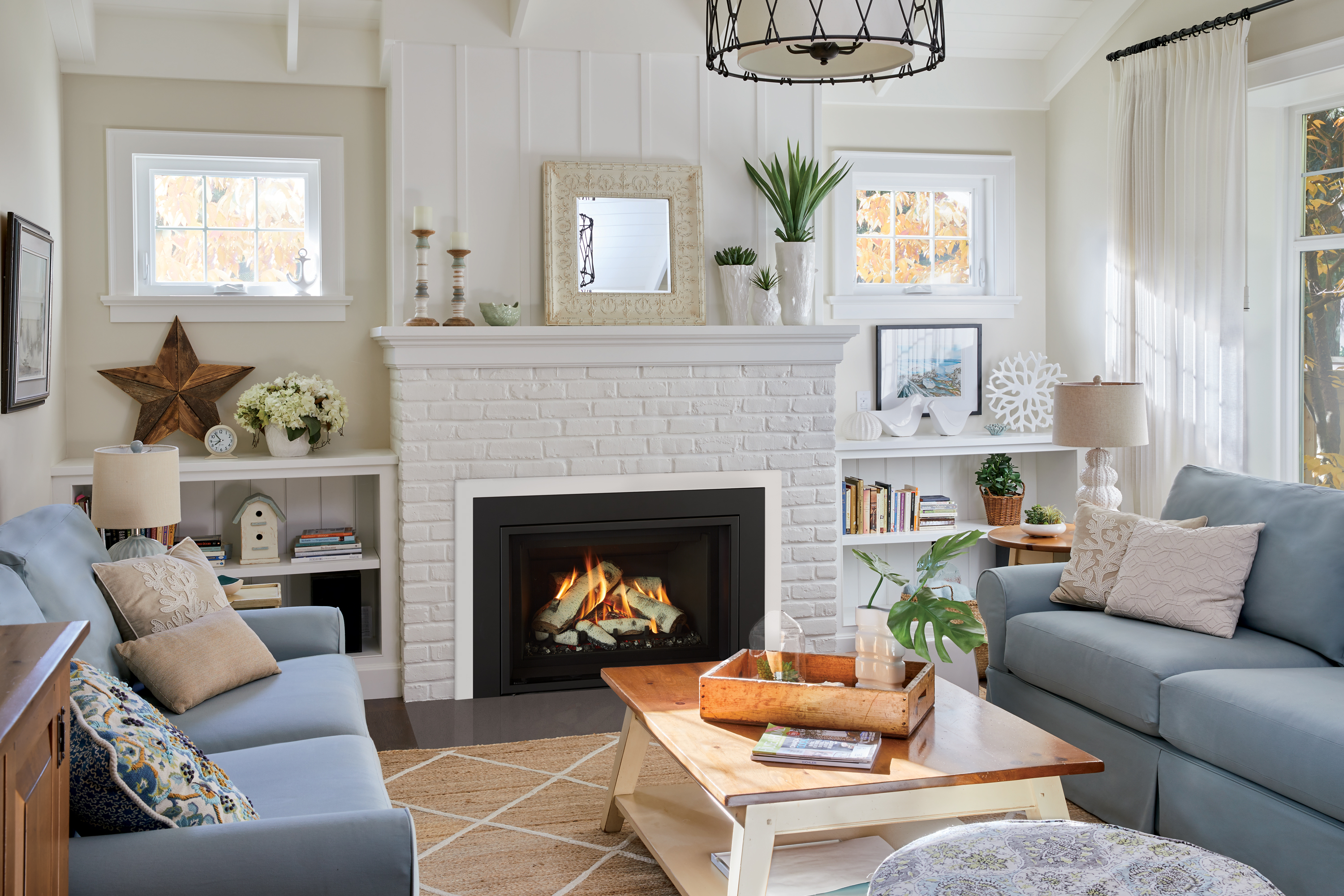 Regency Atmosphere Gi29LE gas insert lit in a bright, airy coastal living room with a white-brick fireplace, blue sofas and built-in bookshelves