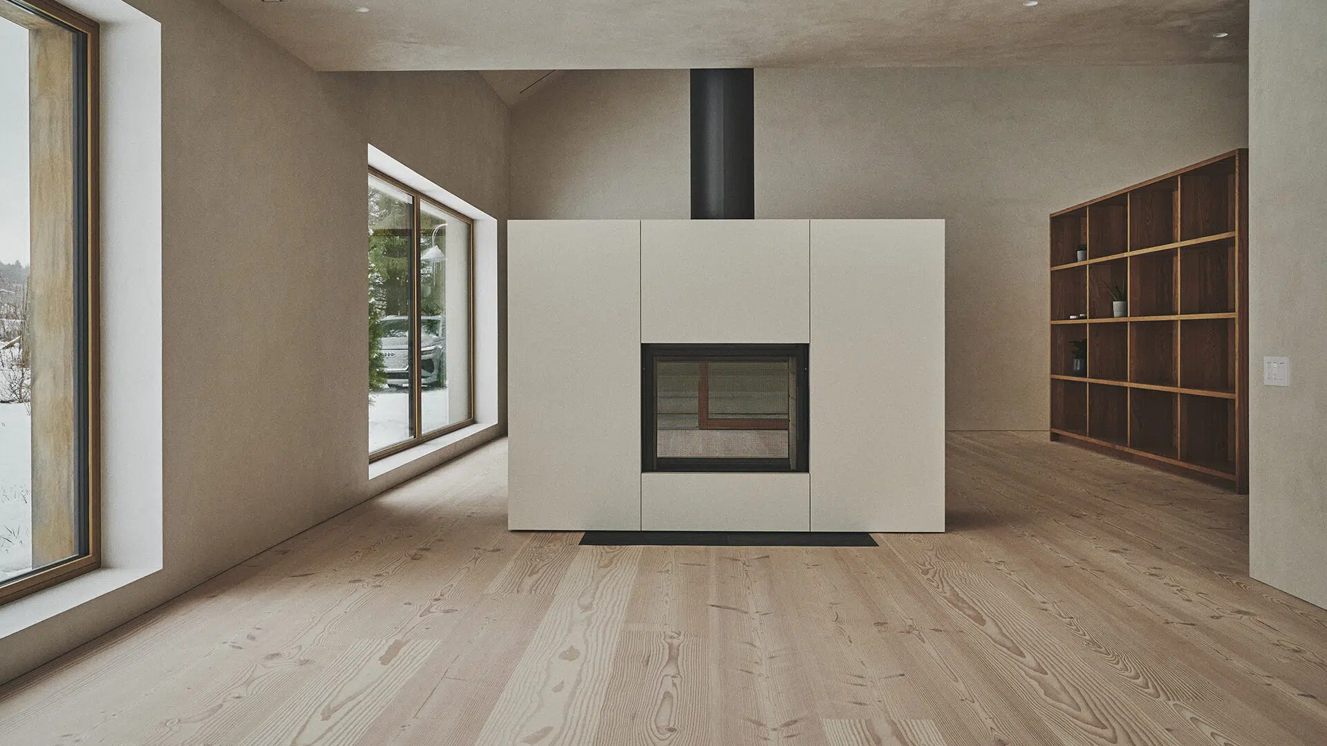 Stûv 21 Clad fireplace in a soft cream finish standing as a clean freestanding block in a minimalist plaster room with wide-plank wood floors and a snowy window view