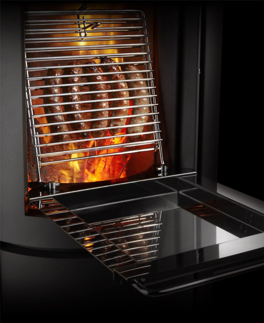 Stuv 30 Compact loading door opened with a stainless grill laid over the fire and sausages cooking above the flames