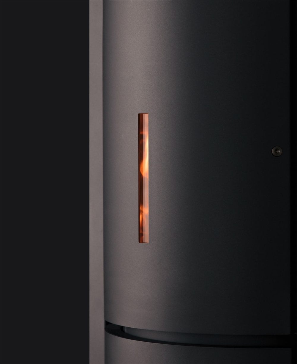 Stuv 30 Compact stove in a darkened room, the black steel drum with a narrow vertical slit glowing orange with fire