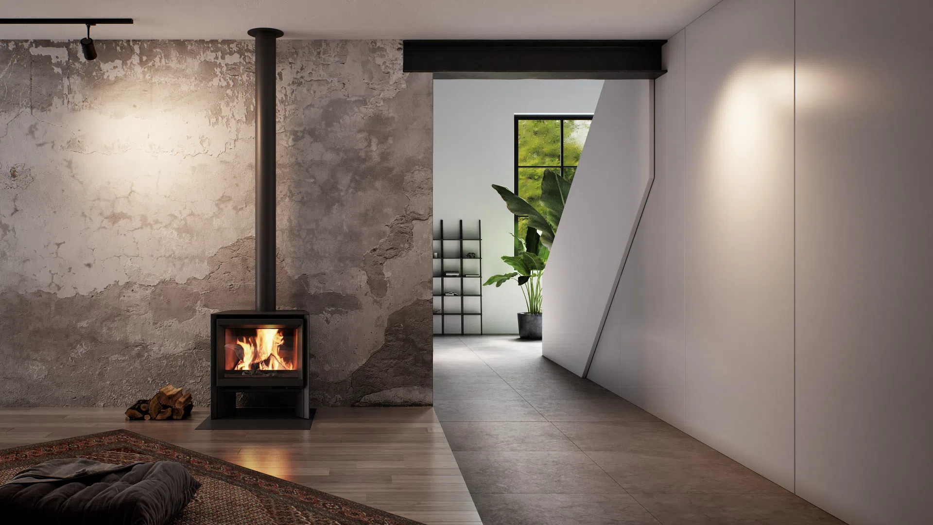 Stûv 6-H wood stove standing against a raw, weathered plaster wall in a modern open-plan room — a compact black steel stove with a wide window of burning logs, a slim black flue rising straight to the ceiling, split firewood stacked on the floor beside it and a patterned rug in the foreground