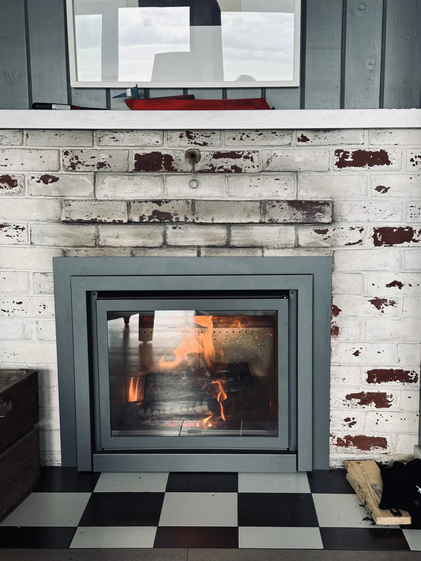 Stûv 16-In retrofit into a heritage painted brick fireplace with chippy white paint showing red brick beneath, checkered tile hearth