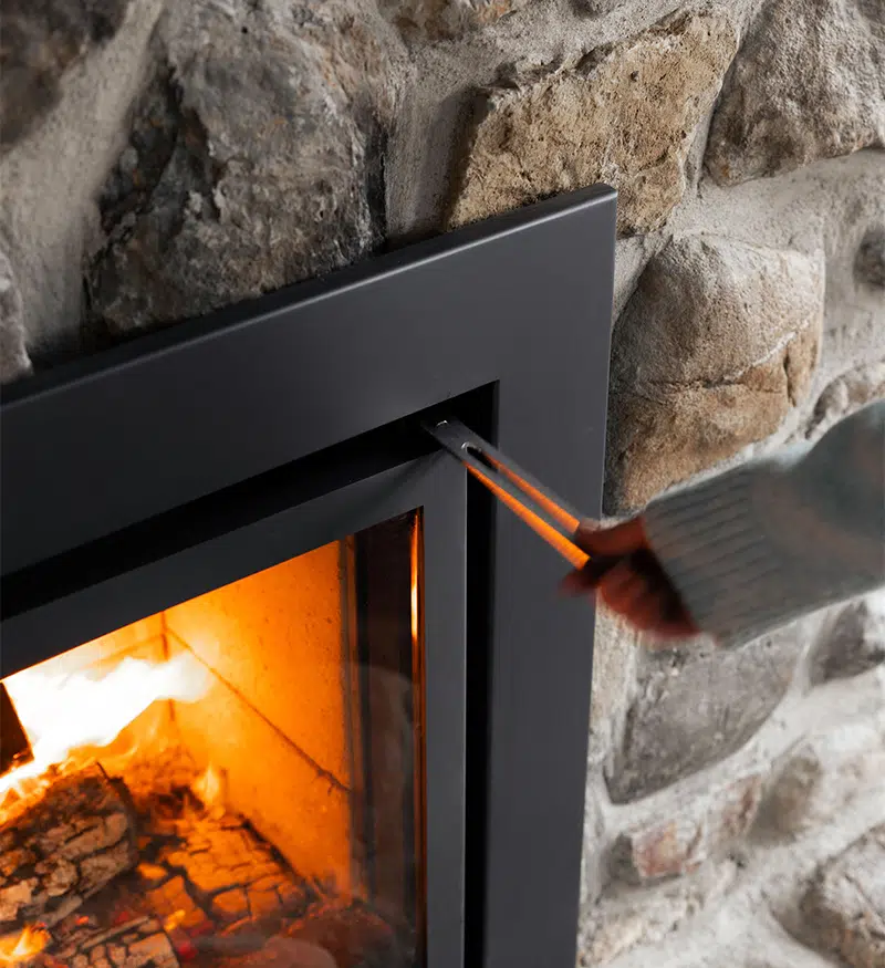 Close-up of the Stûv 16-In door being opened with the discreet removable key, the fire glowing inside against the stone surround