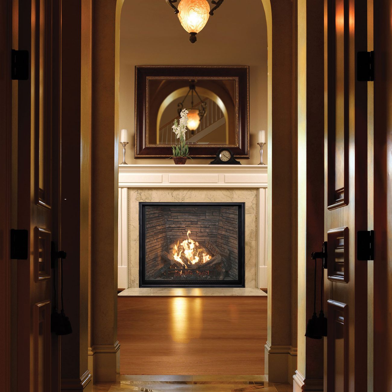 Town & Country TC42 gas fireplace with the Heartwood log set and Madison stone panels, seen down a panelled hallway through an arched opening, set in a marble surround beneath a white mantel with a mirror and candlesticks above