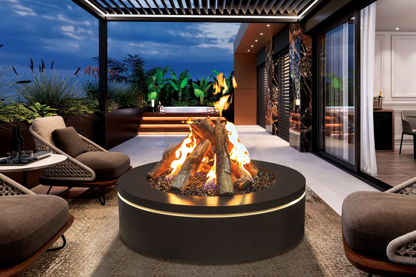 Urbana Halo 40 round gas fire pit in black with a split-log fire over crushed glass and a ring of soft LED light beneath the rim, on a rooftop terrace at dusk with rope-backed chairs, planters and a hot tub beyond