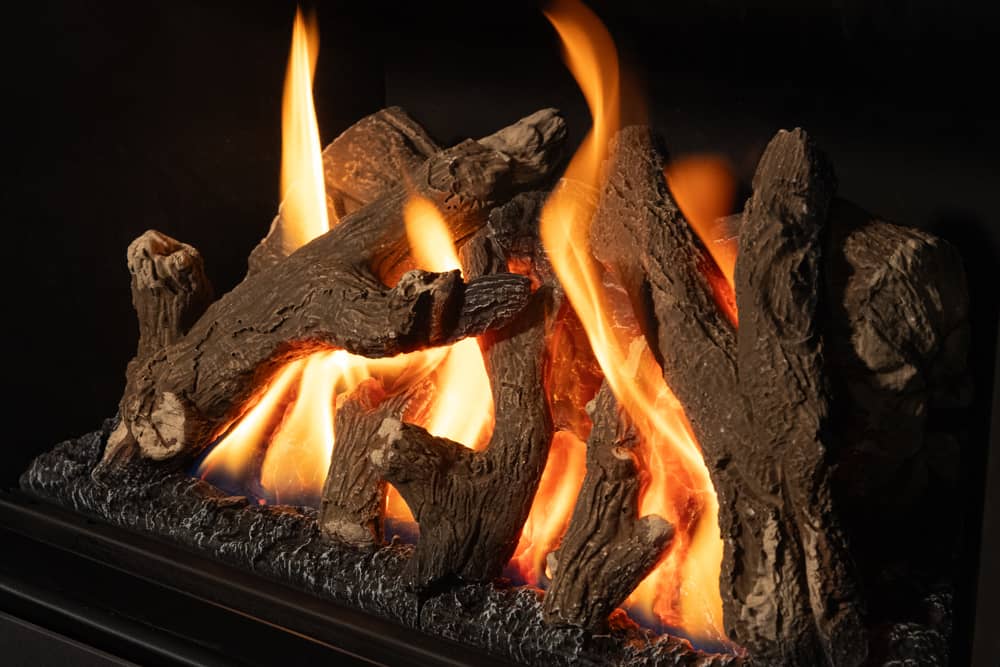 Close view of the Valor G2 traditional log set, bark-textured logs on a bed of glowing embers with orange flames rolling between them