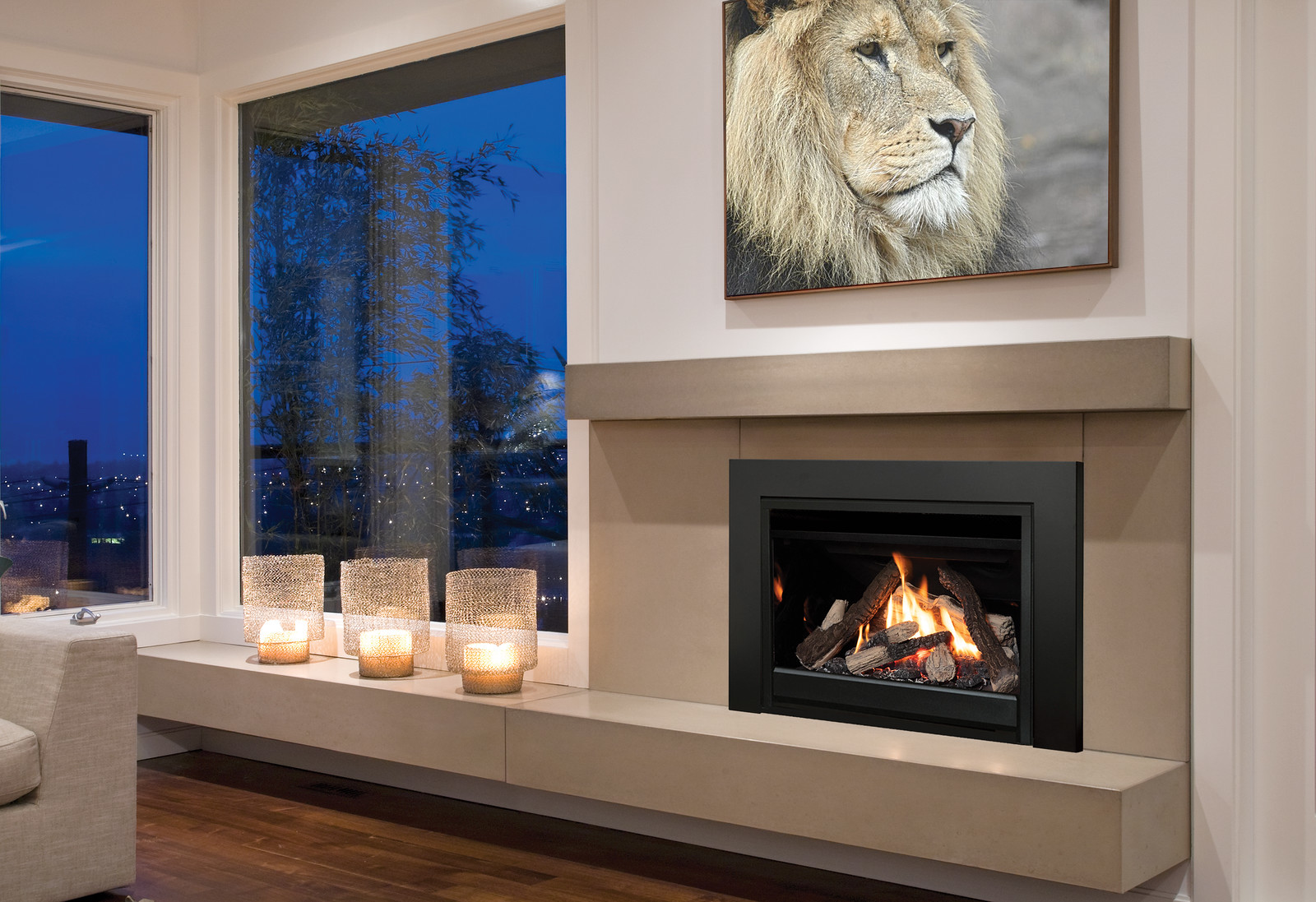 Valor G3 V-Class gas insert glowing in the evening, set into a concrete mantel beside a window with a city view at dusk