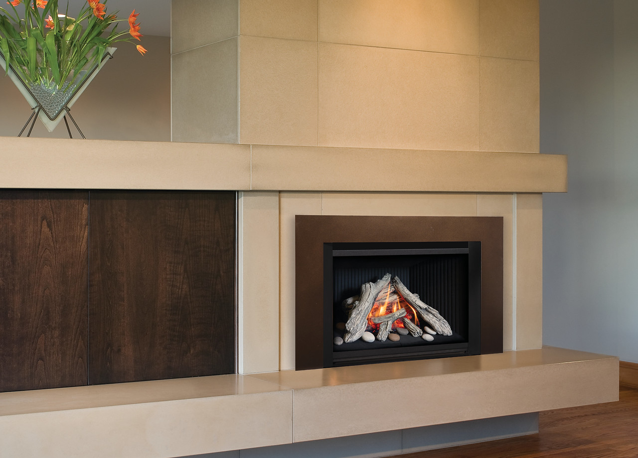 Valor G4 gas insert in a contemporary install with cream stone surround, dark wood paneling, and a driftwood log set on white pebbles