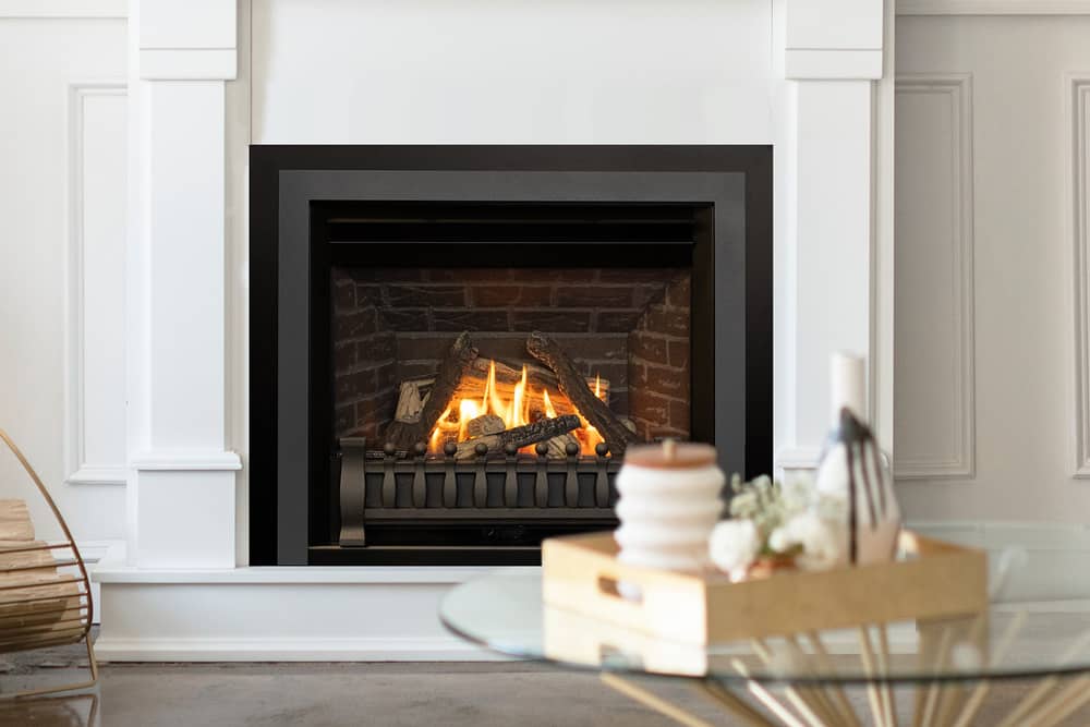 Valor Horizon gas fireplace with logs burning against a red brick liner behind a black front and a low fender, set into a white panelled mantel