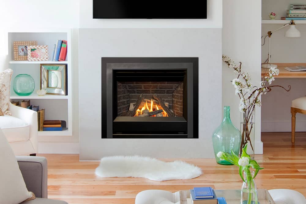 Valor Horizon with traditional logs against a red brick liner, set into a pale surround beneath a wall-mounted television in a bright living room with white shelving