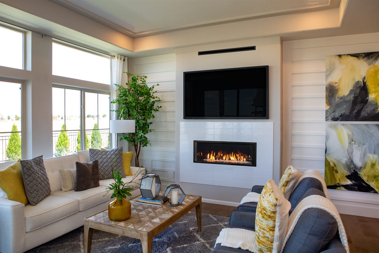 Valor L1 linear gas fireplace set into white textured tile beneath a wall-mounted television, with the slim HeatShift vent visible above the screen, in a bright living room with shiplap walls, a cream sofa and a large abstract painting