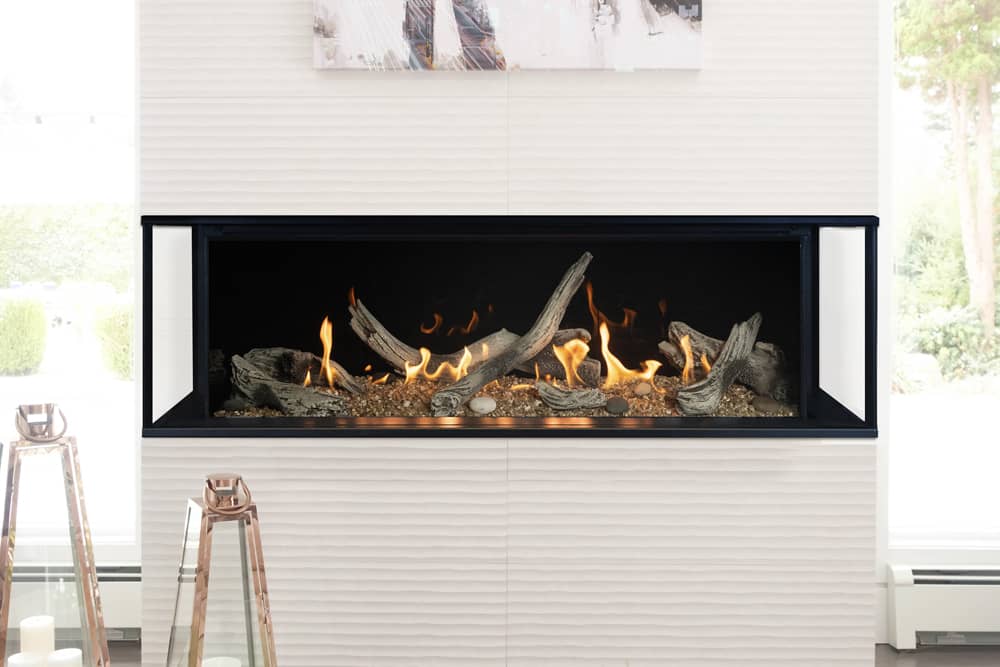 Valor LX2 three-sided gas fireplace with a driftwood log bed set into a rippled white tile wall, glass on the front and both ends, copper lanterns on the floor beside it