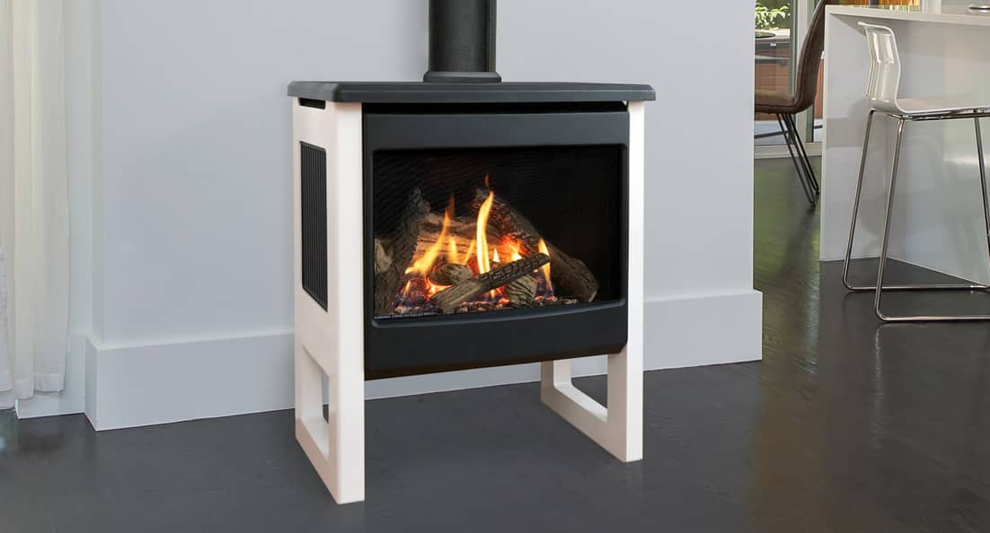 Valor Madrona freestanding gas stove with a black top and firebox and pale legs, a log fire behind the glass and a flue rising to the ceiling